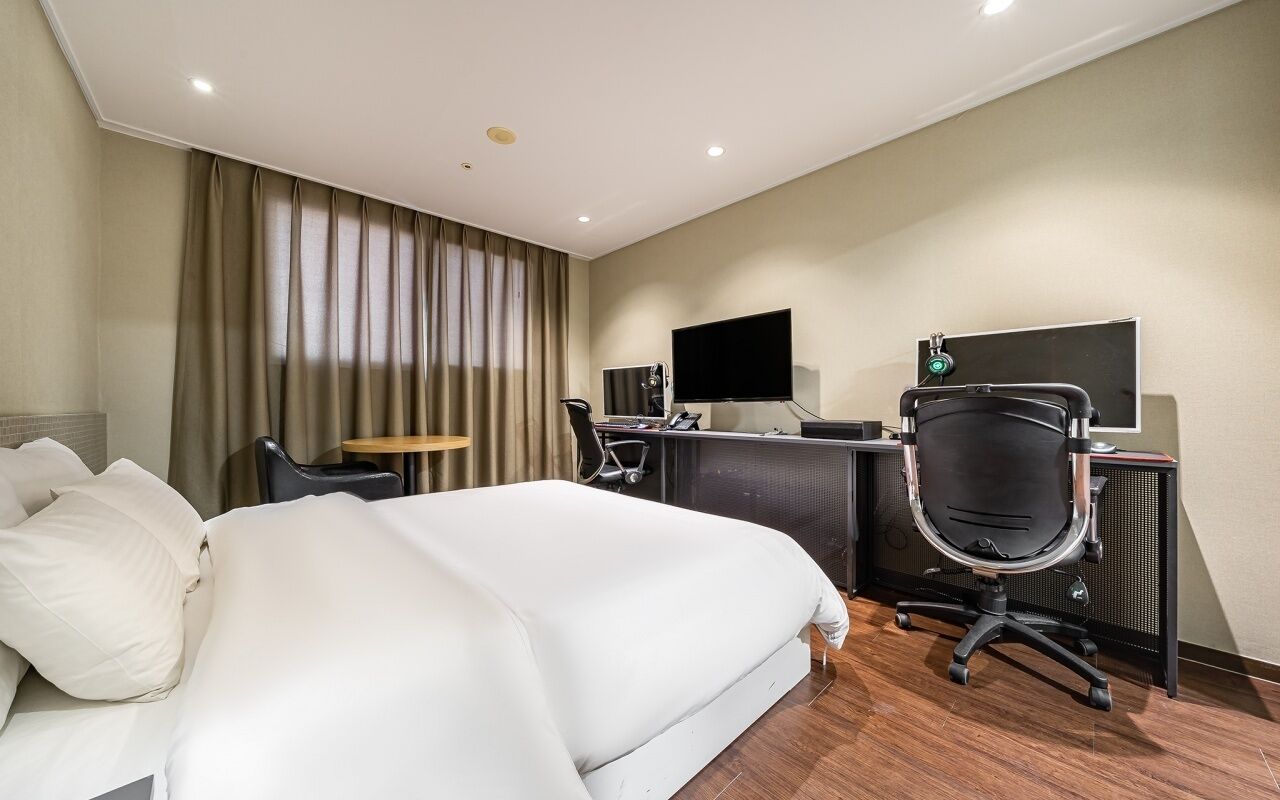 Una habitación de hotel con una cama grande, un escritorio con computadora, una silla y un televisor.