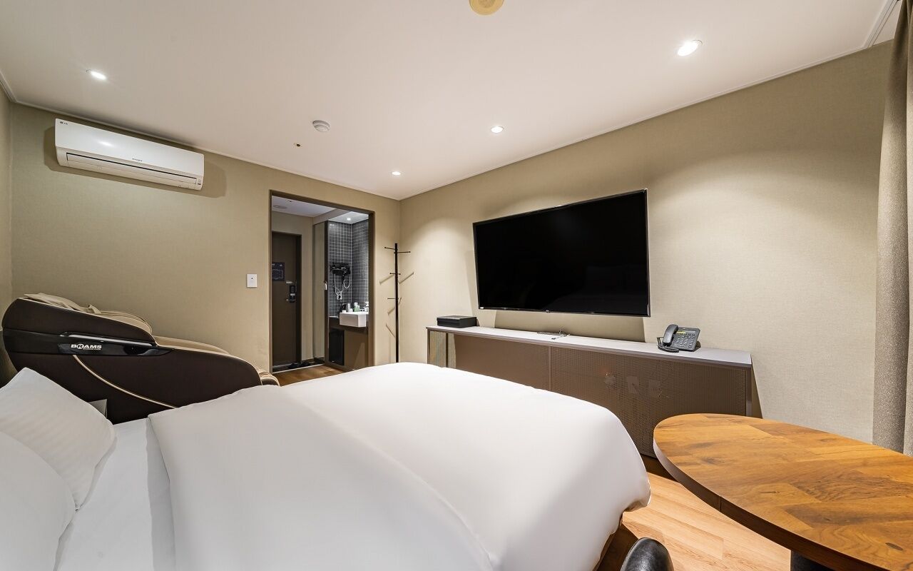 A hotel room with a bed, a desk, a TV, and an air conditioning unit.