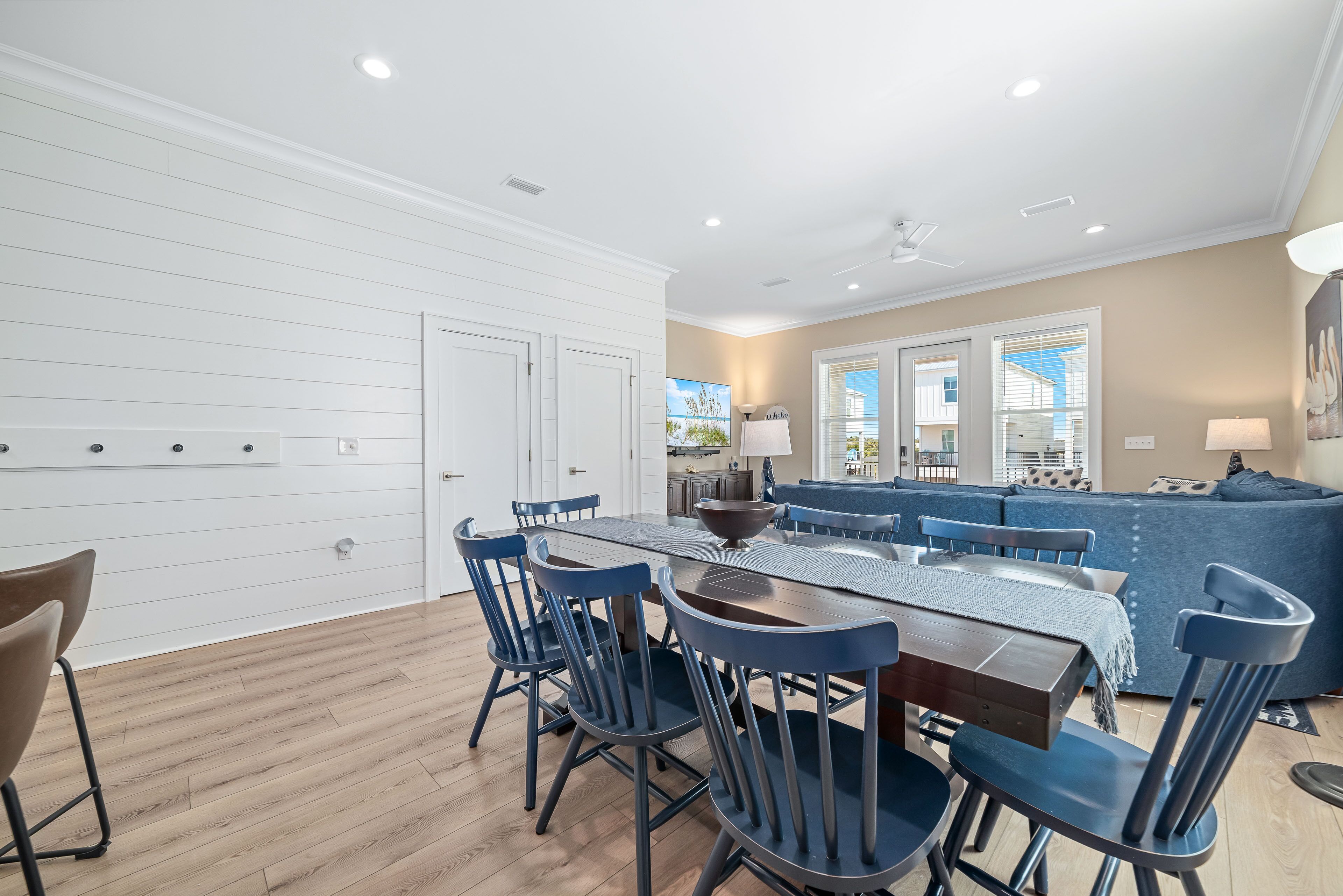 A modern kitchen with white cabinetry, a dining area with a wooden table and blue chairs, and a living area with a blue sofa and beige walls.