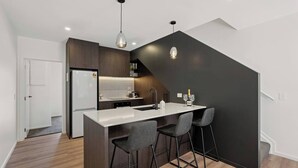 Una cocina moderna con una isla central, taburetes de bar, iluminación colgante y una pared de acento oscura.