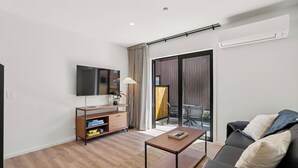 Una sala de estar moderna con un televisor de pantalla plana, un mueble de entretenimiento de madera y un sofá negro.