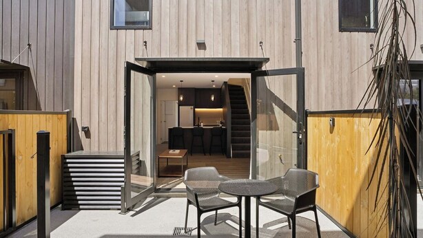 Un edificio moderno con fachada de madera, puerta de entrada de vidrio y un área de cocina visible con una escalera.