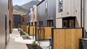 Un edificio residencial moderno con un sendero estrecho, cercas de madera y montañas al fondo.