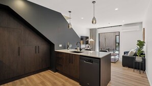 Una cocina moderna con muebles oscuros, lavavajillas y una isla central. Hay un rincón comedor con un sofá y una planta.