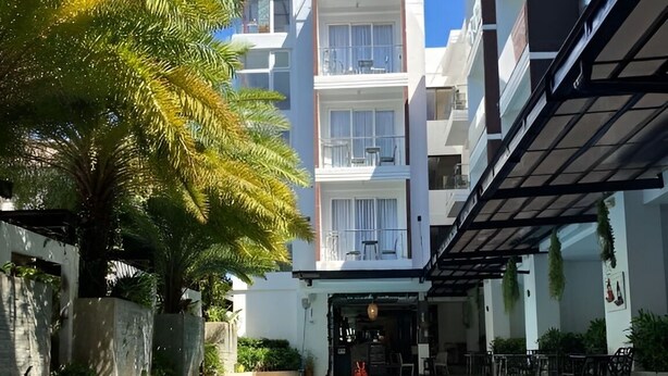 Una piscina de diseño curvo, rodeada de sillas de descanso y un edificio con balcones.