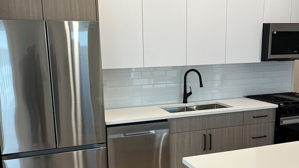 Una cucina moderna con elettrodomestici in acciaio inossidabile, mobili bianchi e una parete di fondo rivestita di piastrelle.