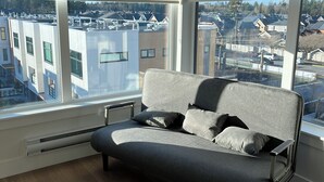 Un soggiorno moderno con un divano grigio, un termosifone e ampie finestre con vista sulla città.