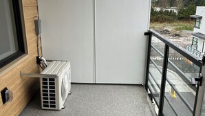 Un balcone con pavimento piastrellato grigio, un condizionatore d'aria bianco e vista su un'area di parcheggio con auto rosse.