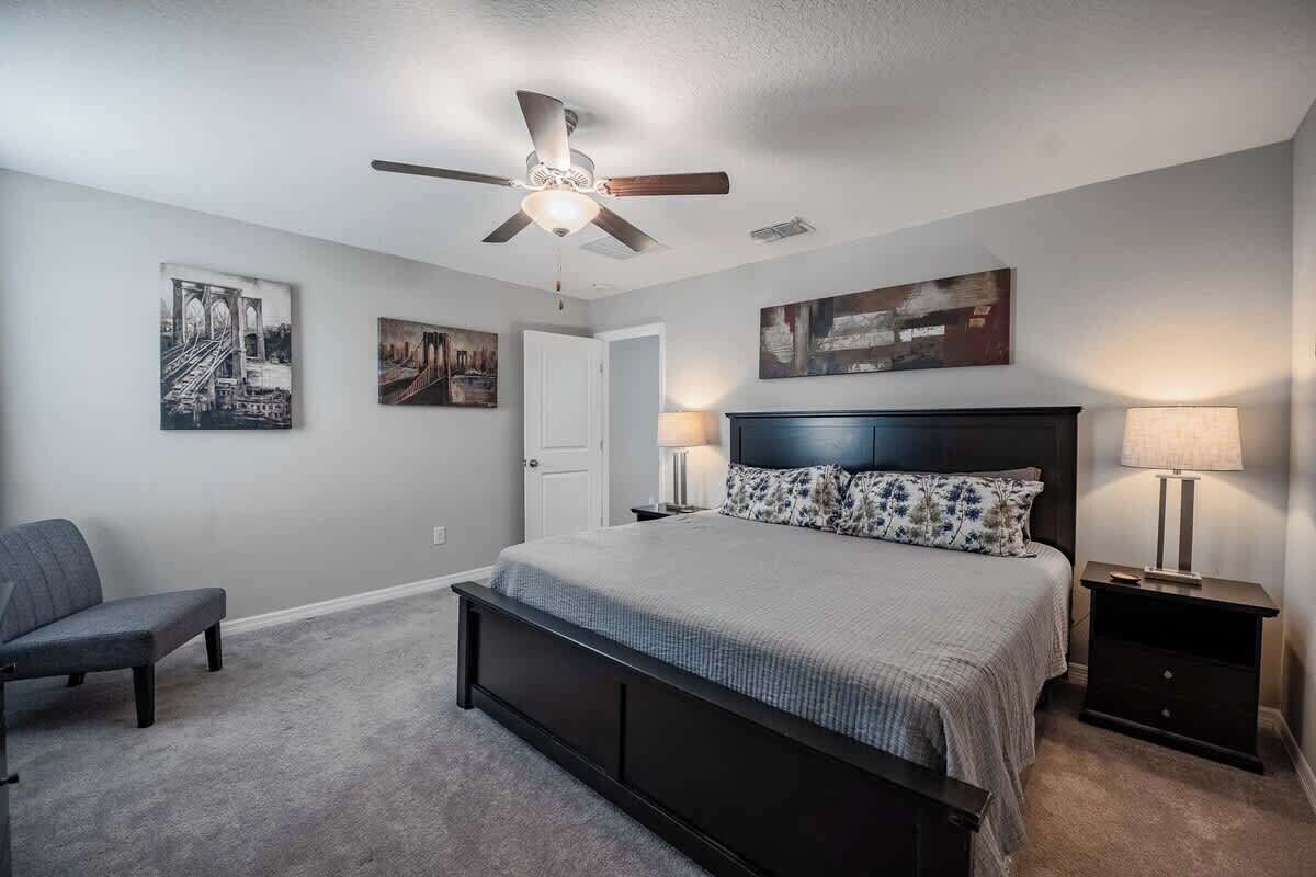 Une chambre à coucher avec un lit, une chaise, un ventilateur de plafond et des œuvres d’art accrochées aux murs.