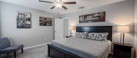 Une chambre à coucher avec un lit, une chaise, un ventilateur de plafond et des œuvres d’art accrochées aux murs.