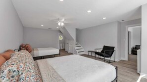 A modern bedroom with a large bed, a chair, and a staircase leading to another room. - 5BR Historic Home | Sleeps 14 | Lake Hollingsworth (Lakeland)