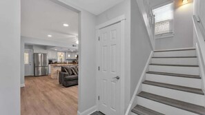 A modern kitchen with stainless steel appliances, a dining area with a gray sofa, and a staircase with wooden steps. - 5BR Historic Home | Sleeps 14 | Lake Hollingsworth (Lakeland)