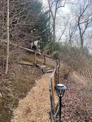 Eine Holztreppe führt einen Hügel hinauf, umgeben von Bäumen und einem Holzzaun.