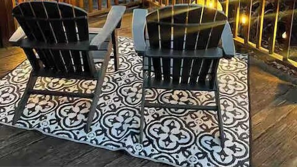 Um terraço com duas cadeiras e uma mesa, rodeado por um corrimão com luzes de fadas, com vista para uma área arborizada e montanhas ao longe.
