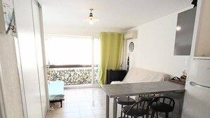 Una cocina moderna con comedor, un balcón con cortina verde y suelo de baldosas.