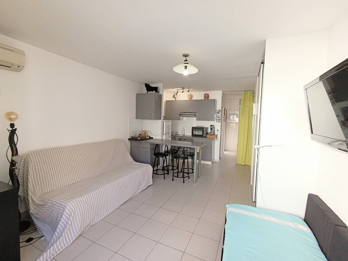 Ett kompakt bostadsutrymme med ett litet kök, en soffa, en matplats och en tv som är monterad på väggen.