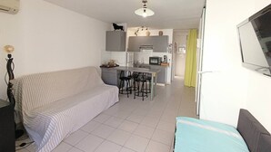 Un espacio habitable compacto con kitchenette, un sofá, un comedor y un televisor instalado en la pared.