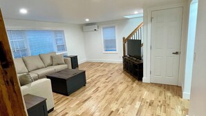 A spacious living room with a wooden floor, a sofa, a coffee table, and a TV. There is a staircase leading to another level.