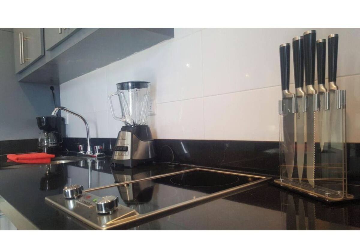 Eine Küche mit schwarzem Arbeitsplatz, einer Kaffeemaschine, einem Mixer und einem Messerblock.