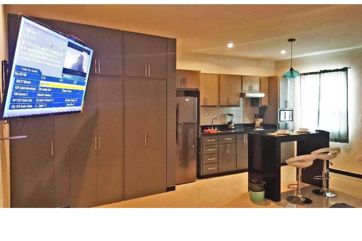 Eine moderne Küche mit Kochinsel, dunklen Schränken und einem an der Wand befestigten Flachbildfernseher.