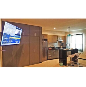 A modern kitchen with a central island, dark cabinets, and a flat-screen TV mounted on the wall.