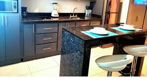 A modern kitchen with dark cabinets, a black countertop, a built-in stove, and a refrigerator. - PRIVATTO SUITES (Saltillo)