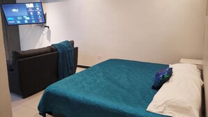 A bedroom with a bed, a TV mounted on the wall, and a small seating area. - PRIVATTO SUITES (Saltillo)