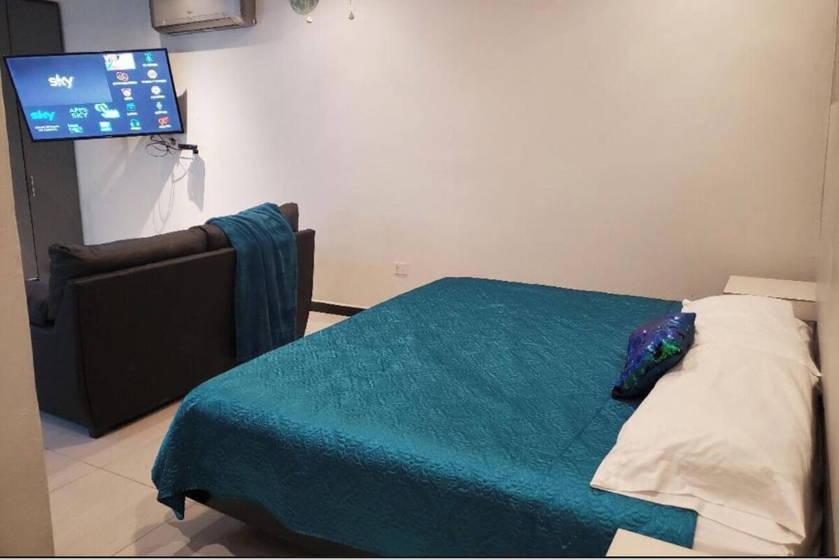 Ein Schlafzimmer mit einem Bett, einem an der Wand montierten Fernseher und einer kleinen Sitzecke.