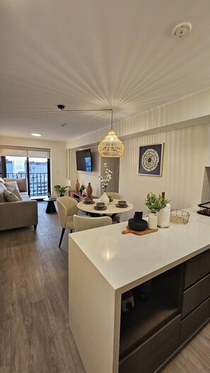 A modern kitchen with a central island, dining area with chairs, a sofa, and a TV mounted on the wall. - Luxury 3-Bedroom Urban Retreat, Prime Walkable Location with Pool (Miraflores)