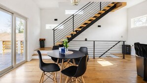 Eine moderne Küche mit einer Holztreppe, einem Essbereich mit schwarzen Stühlen und einem großen Fenster, das natürliches Licht hereinlässt.