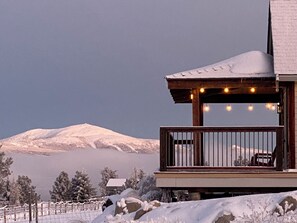 Ein Holzbalkon mit Geländer, der auf eine verschneite Landschaft und einen Berg Blick bietet.