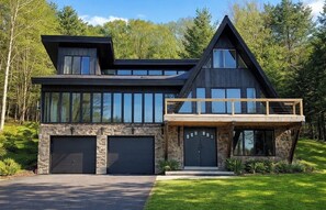A modern two-story house with a stone facade, large windows, and a prominent gable roof. - South Shore Chalet-Lake View with Docks- Family Friendly (Northville)
