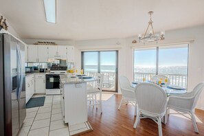 A modern kitchen with white cabinets, a refrigerator, and a dining area with white chairs and a table. - Panorama Beach House Gulf Front Sleeps 12 (Panama City Beach)
