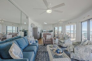 A spacious living area with a large sofa, armchairs, and a coffee table. There is a kitchen in the background, and large windows provide a view of the ocean. - Panorama Beach House Gulf Front Sleeps 12 (Panama City Beach)