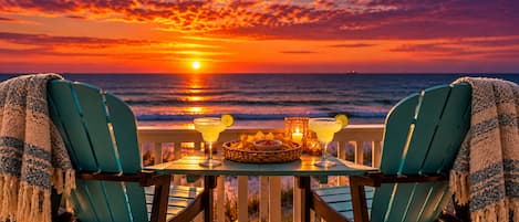 Zonsondergang vanaf een balkon met twee stoelen, een tafel met een drankje en een mand met snacks.