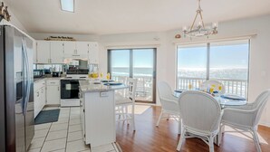 Une cuisine moderne avec des meubles blancs, un réfrigérateur et un coin repas comprenant des chaises et une table, le tout dans des tons blancs.