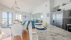 Une cuisine spacieuse avec un grand îlot central, un coin repas avec des chaises blanches et un salon doté d’un canapé bleu.