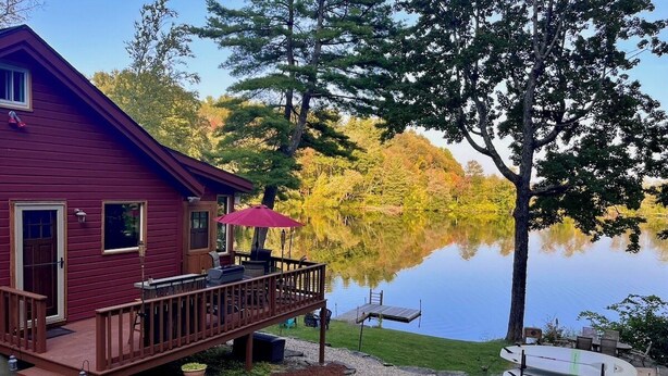 A red cabin with a deck overlooking a lake, surrounded by trees and a dock. - Kayak on Prospect Lake, Paddle Boards, Swim Dock+! (Egremont)