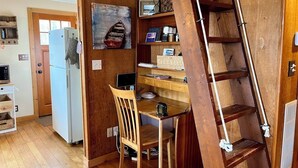 A compact kitchen with wooden cabinetry, a white refrigerator, a wooden dining table with a chair, and a wooden ladder. - Kayak on Prospect Lake, Paddle Boards, Swim Dock+! (Egremont)