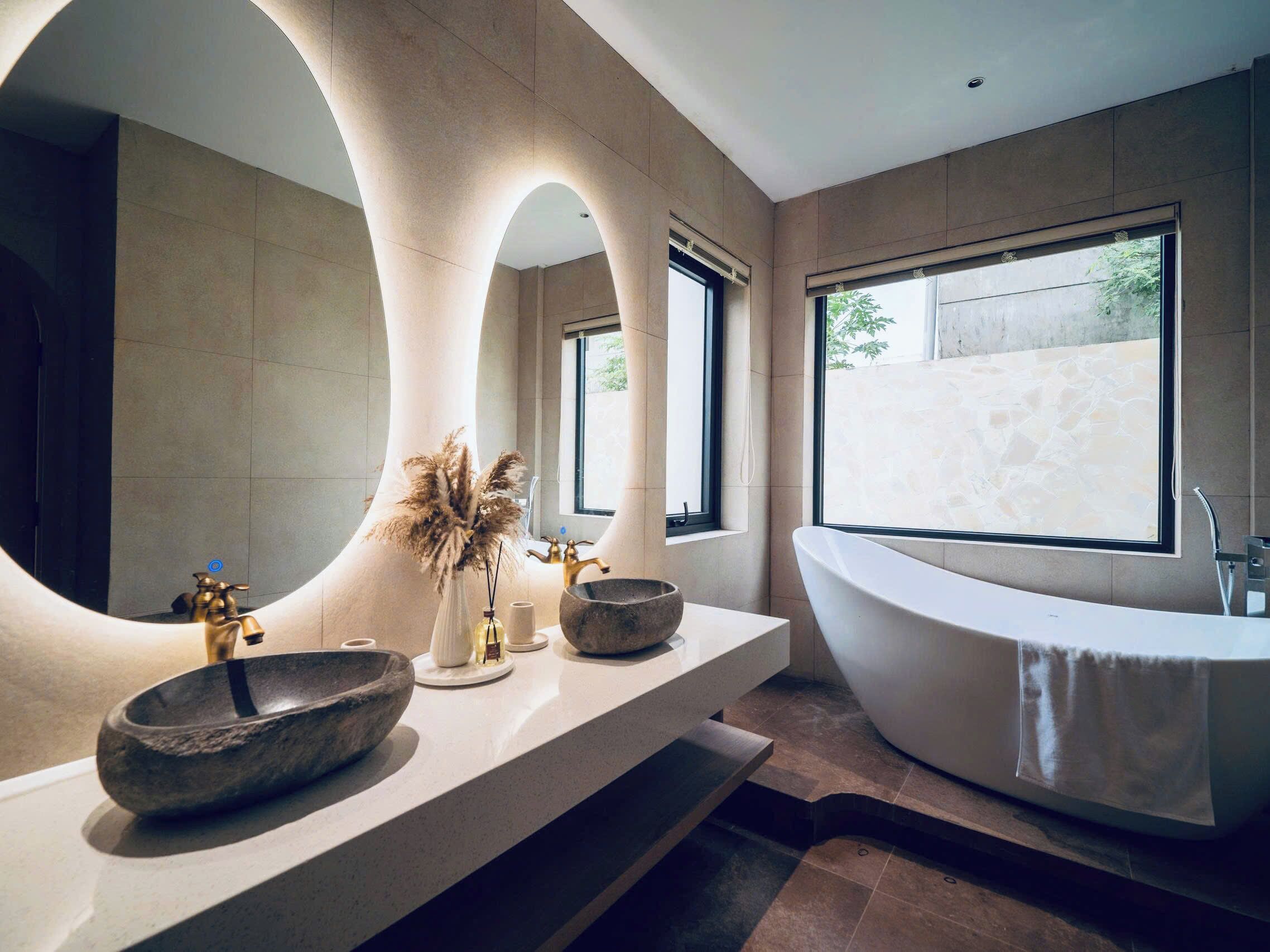 A modern bathroom with a freestanding bathtub, a large mirror, and a window providing natural light.
