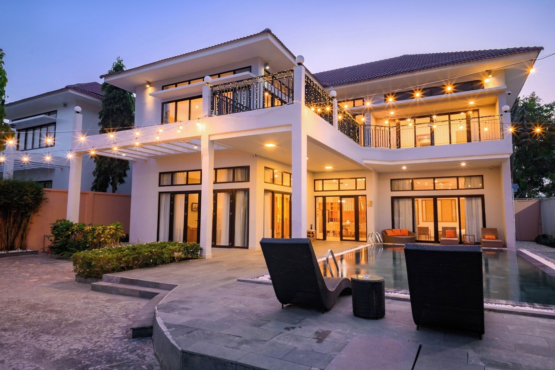 A two-story house with a swimming pool, outdoor seating, and string lights.