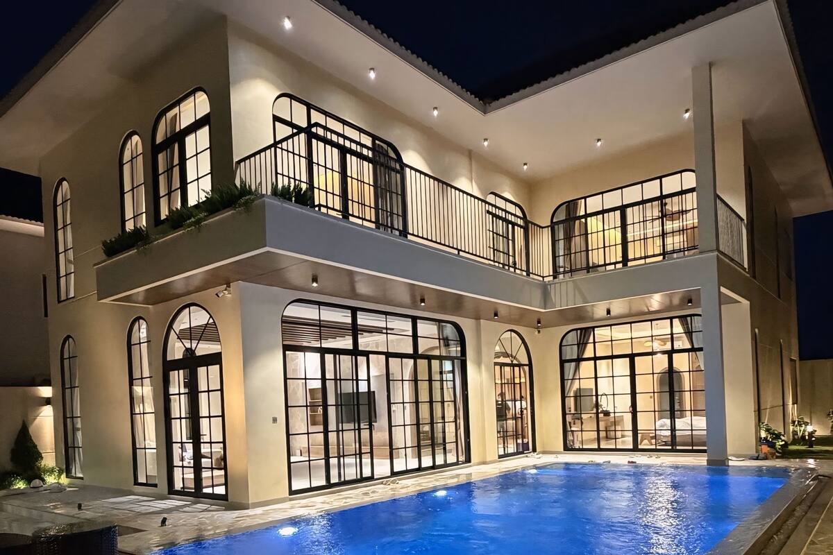 A two-story house with a swimming pool, large windows, and a balcony.
