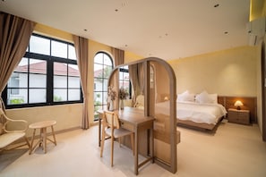 A bedroom with a bed, bedside table, desk, chair, and a window with curtains.
