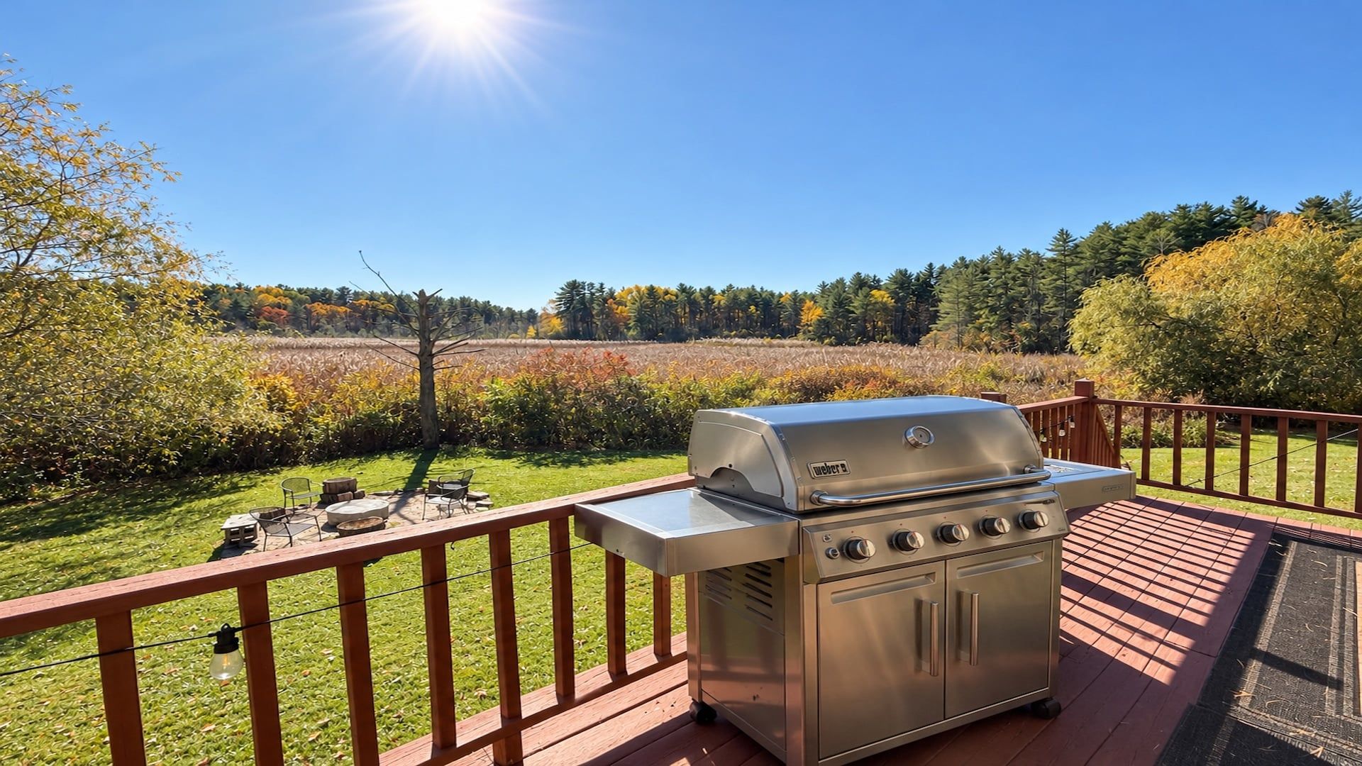 Un barbecue installé sur une terrasse en bois, avec vue sur un champ et des arbres.