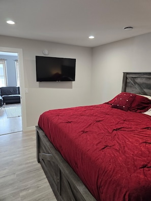 Une chambre à coucher avec un lit, un téléviseur fixé au mur et une porte donnant sur une autre pièce.