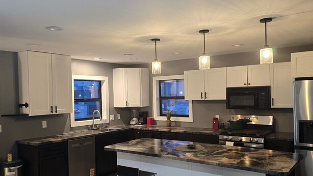 Una cocina moderna con una isla central, electrodomésticos de acero inoxidable e iluminación colgante.