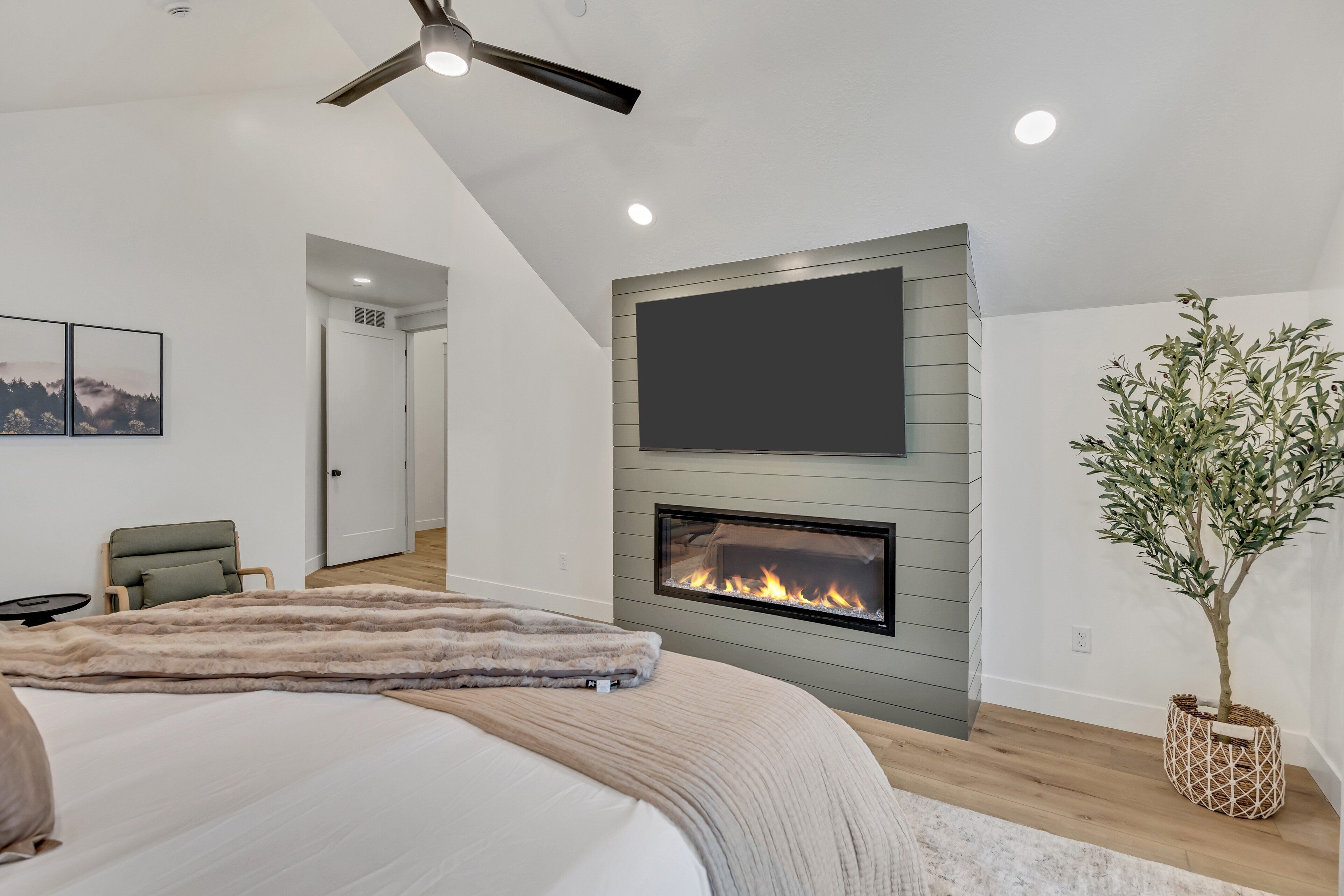 Une chambre moderne dotée d’une cheminée, d’un ventilateur de plafond et d’un grand téléviseur fixé au mur.