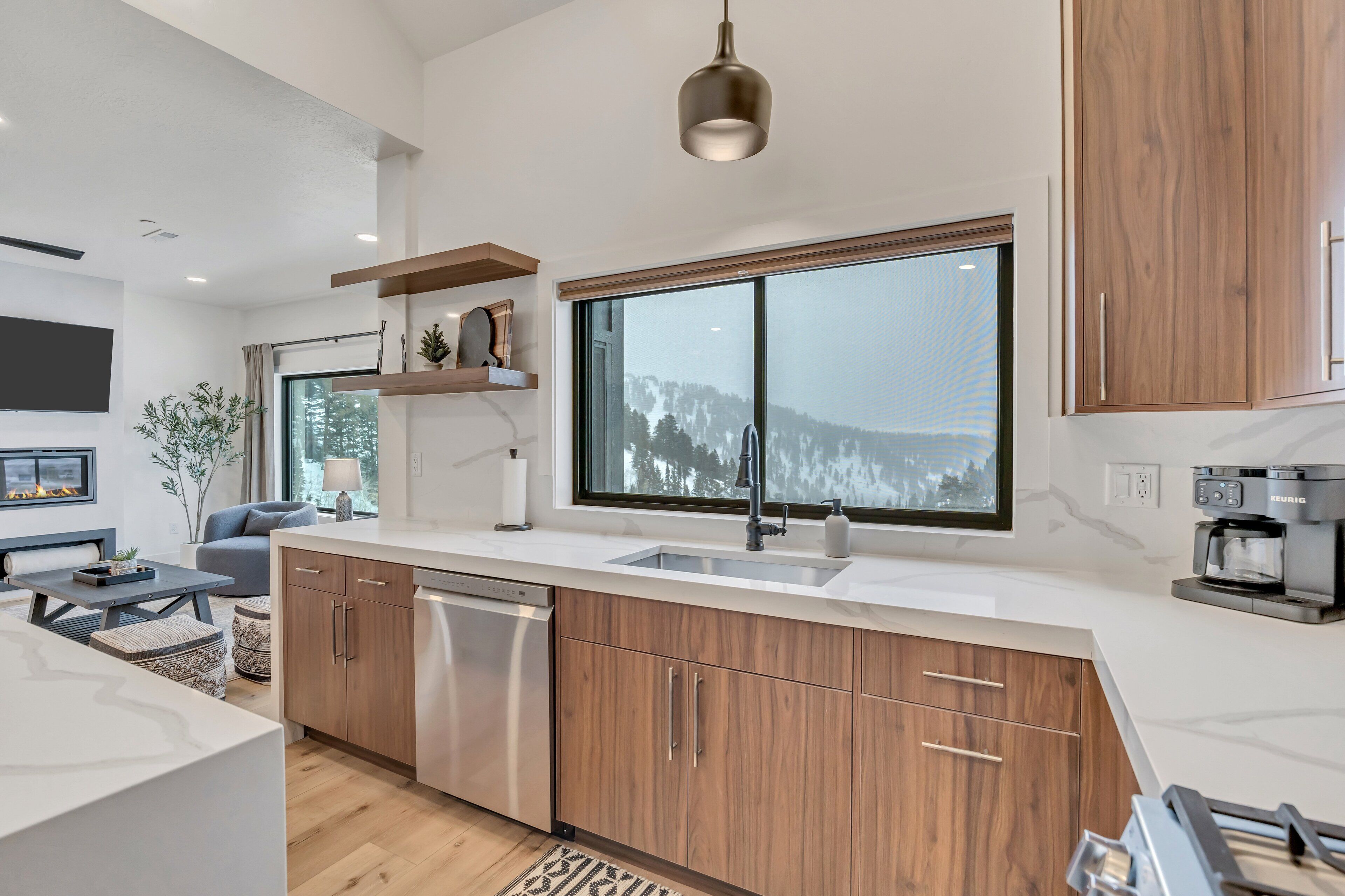 A modern kitchen with wooden cabinets, a large window, and a built-in dishwasher.
