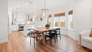 A spacious kitchen with a wooden dining table and chairs, a chandelier, and large windows with blinds. - Private Pool, Coastal Cottonwood Retreat, Sleeps 13,  Beach Access (Inlet Beach)