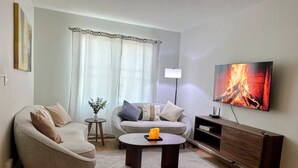 A modern living room with a sofa, armchair, coffee table, TV, and a fireplace image on the wall. - Casa Luma is a calm, light-filled home designed for rest and simplicity. (Aguascalientes)